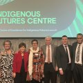 A group of men and women stand side by side on stage with a slide behind them reading Indigenous Futures Centre.